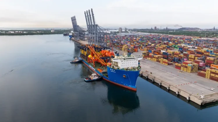 Puerto de carga en Michoacán con contenedores y grúas en el muelle, barcos y almacenes de mercancías en el fondo.