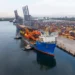Puerto de carga en Michoacán con contenedores y grúas en el muelle, barcos y almacenes de mercancías en el fondo.