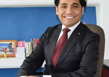 Hombre de negocios en traje formal en oficina con libros y decoraciones en el fondo.