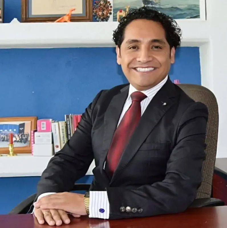 Hombre de negocios en traje formal en oficina con libros y decoraciones en el fondo.