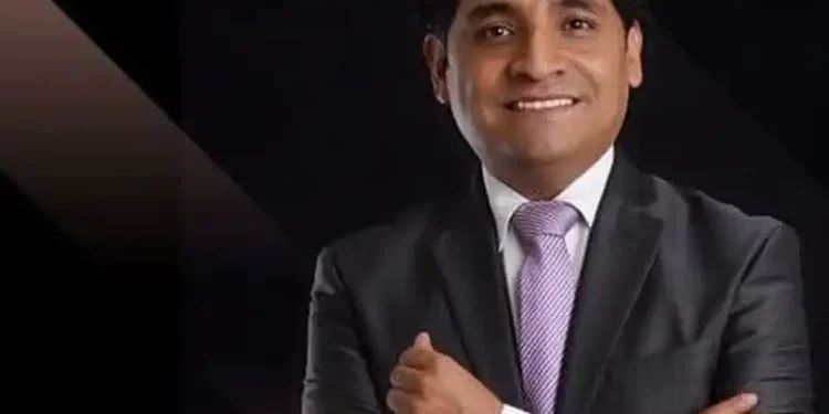 Académico mexicano en traje formal recibe reconocimiento en Caracas, Venezuela, con fondo oscuro y expresión de satisfacción.