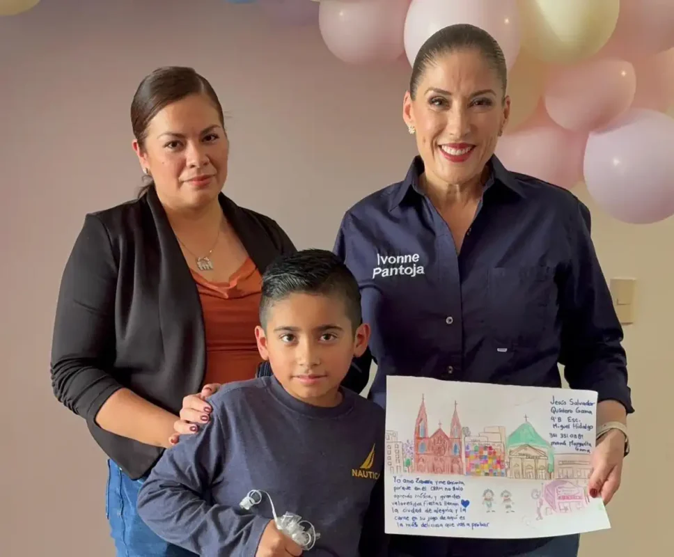 Niña y dos mujeres sosteniendo un dibujo en un evento infantil en Michoacán.