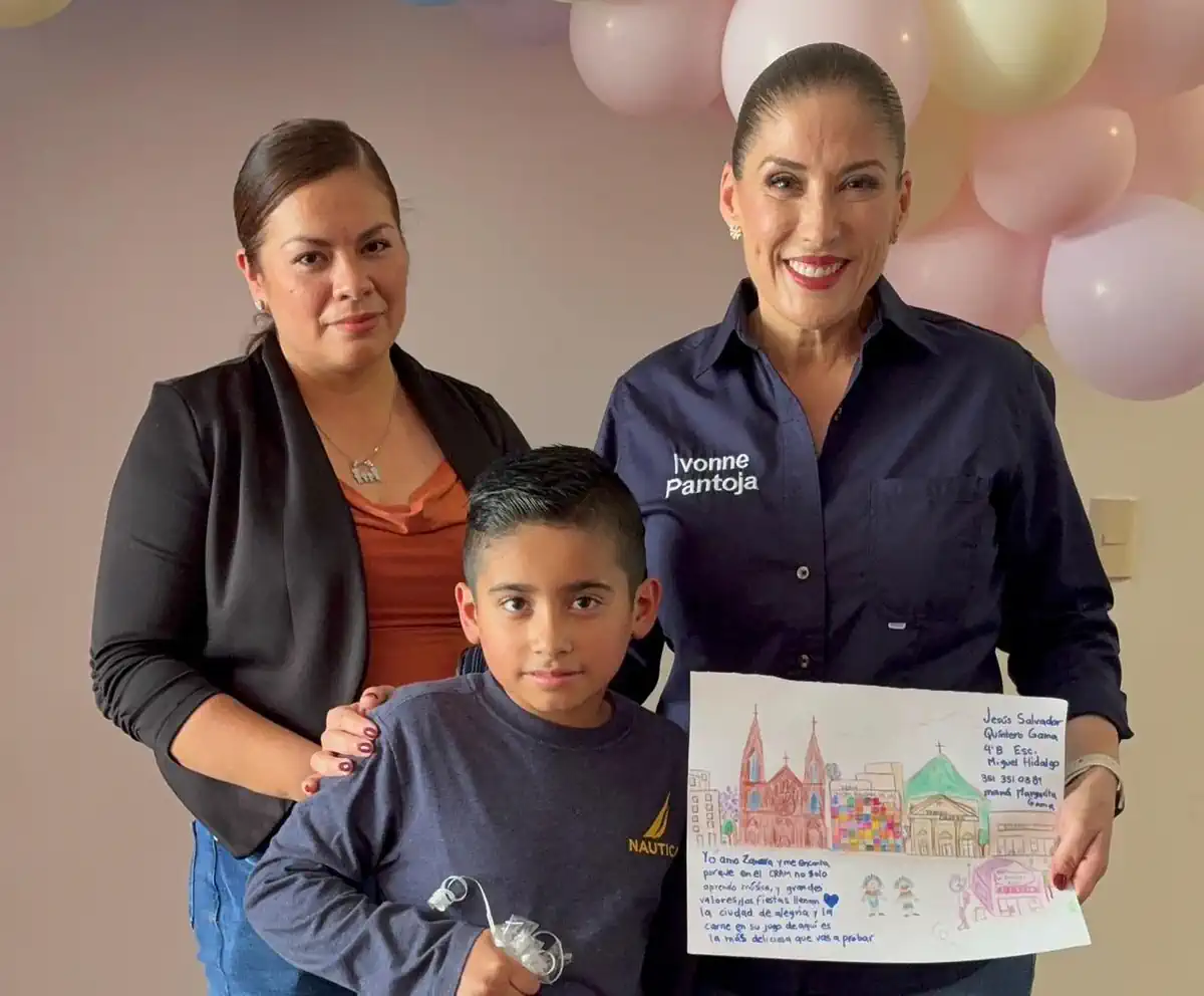 Niña y dos mujeres sosteniendo un dibujo en un evento infantil en Michoacán.