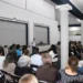 Conferencista en un taller de tanatología frente a una audiencia en un auditorio.