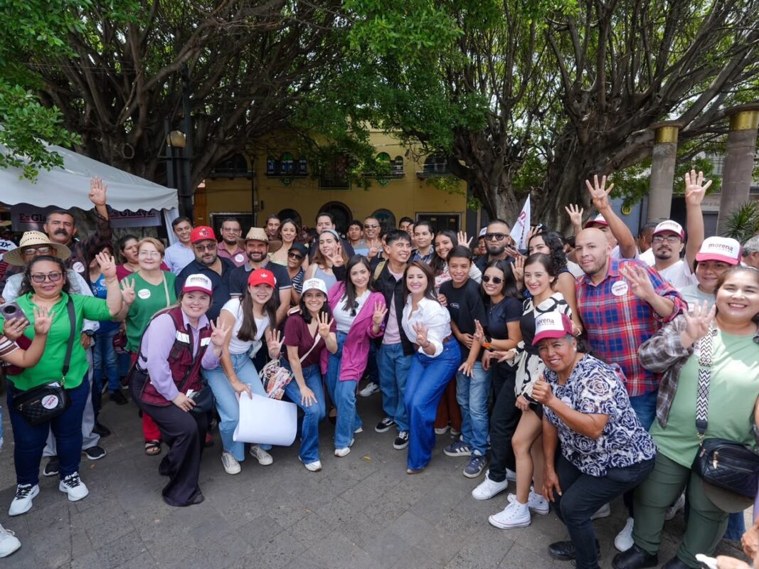 Grupo de personas en evento comunitario con árboles y carpas en fondo, participando en actividad social.