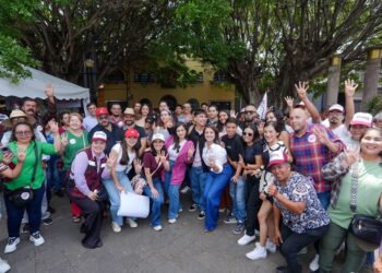 Grupo de personas en evento comunitario con árboles y carpas en fondo, participando en actividad social.