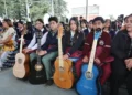 Jóvenes con guitarras en evento escolar en Michoacán, en un espacio cubierto con árboles visibles al fondo.