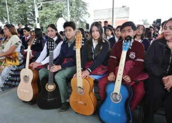 Jóvenes con guitarras en evento escolar en Michoacán, en un espacio cubierto con árboles visibles al fondo.