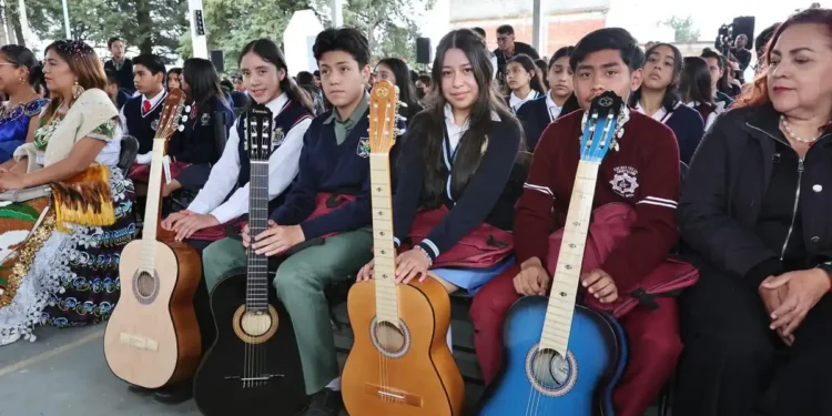 Jóvenes con guitarras en evento escolar en Michoacán, en un espacio cubierto con árboles visibles al fondo.