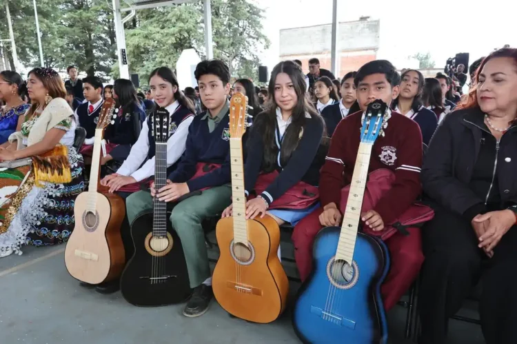 Jóvenes con guitarras en evento escolar en Michoacán, en un espacio cubierto con árboles visibles al fondo.
