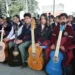 Jóvenes con guitarras en evento escolar en Michoacán, en un espacio cubierto con árboles visibles al fondo.