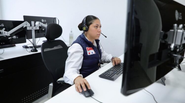 Mujer en centro de atención telefónica con auriculares y computadora, monitoreando llamadas para prevenir extorsiones.