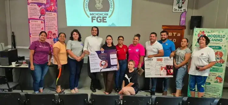 Grupo de personas en una capacitación sobre protección animal en Tepalcatepec, con carteles informativos y pantalla en fondo.