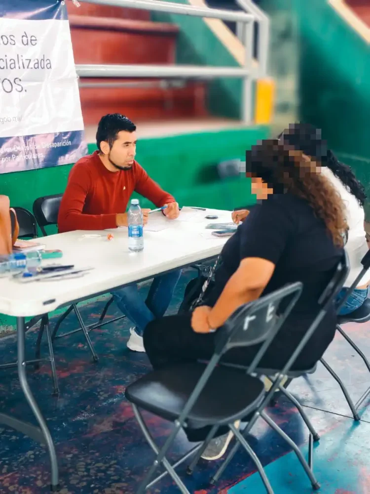 Joven realiza toma de muestras de ADN a mujer en evento en Sahuayo, con fondo de escaleras y banner informativo.