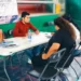 Joven realiza toma de muestras de ADN a mujer en evento en Sahuayo, con fondo de escaleras y banner informativo.
