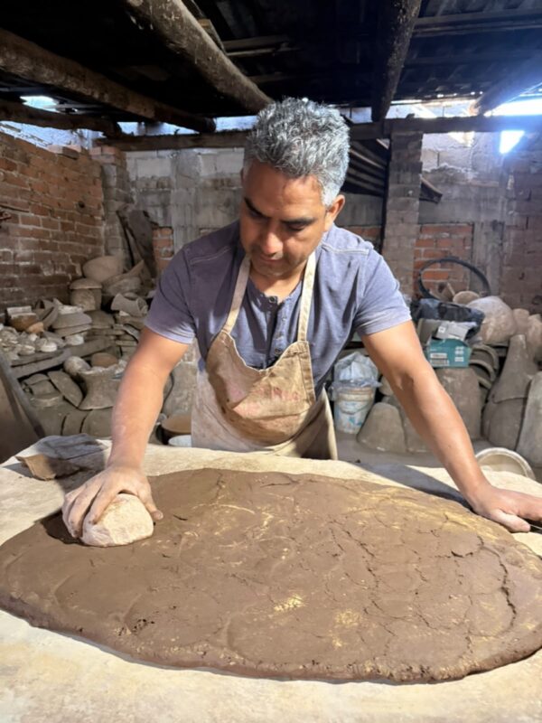 Hombre artesano trabajando en molde de cerámica en taller rústico con ladrillos y herramientas.