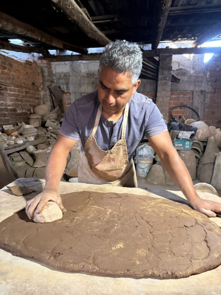 Hombre artesano trabajando en molde de cerámica en taller rústico con ladrillos y herramientas.