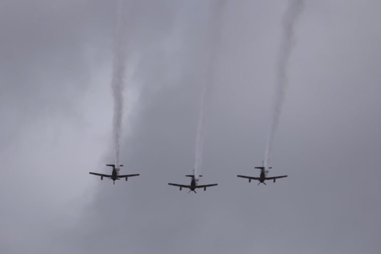 Tres aviones vuelan en formación dejando estelas de humo en un cielo nublado.