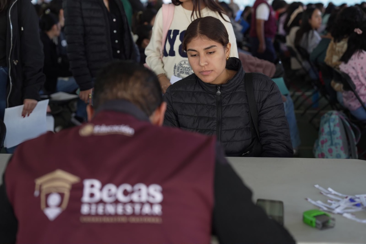 Joven en fila en proceso de solicitud de beca en Michoacán, con personal de apoyo y documentos en mano.