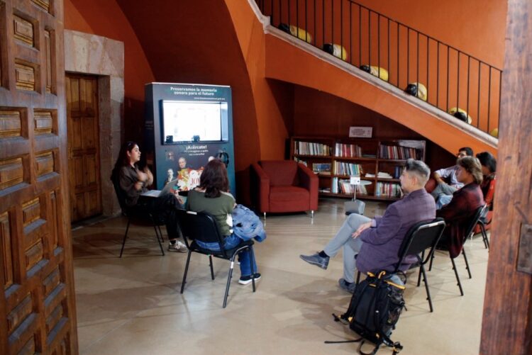 Grupo de personas en una sala de conferencias viendo una presentación en una pantalla digital.
