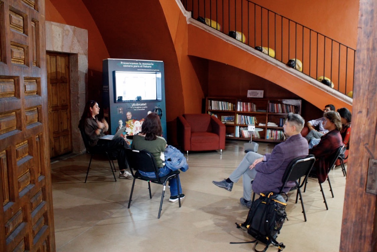 Grupo de personas en una sala de conferencias viendo una presentación en una pantalla digital.