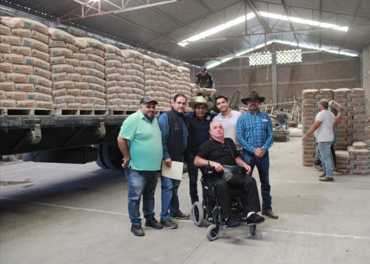 Grupo de personas en almacén de cemento con sacos apilados y maquinaria en segundo plano.