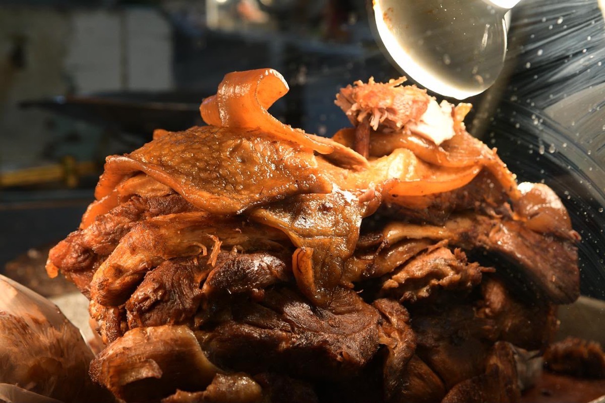 Un gran trozo de carne cocida con piel y grasa apilada bajo una luz brillante.