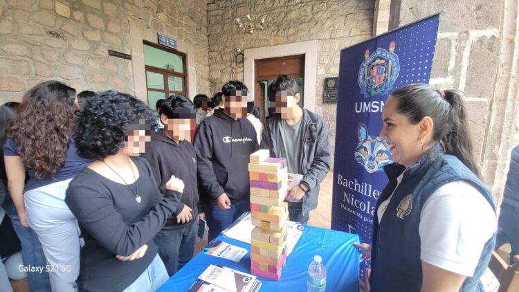 Estudiantes y una representante de la UMSNH juegan Jenga en un evento académico.