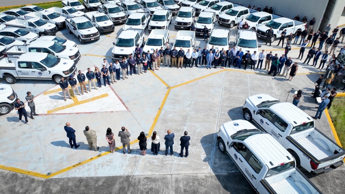 Grupo de funcionarios y policías en ceremonia de entrega de vehículos oficiales en un estacionamiento.