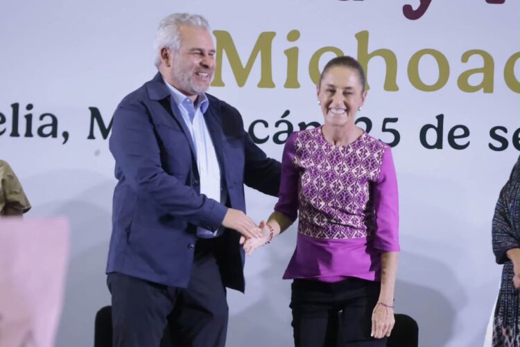 Hombre y mujer en evento oficial en Michoacán, estrechándose la mano y sonriendo.