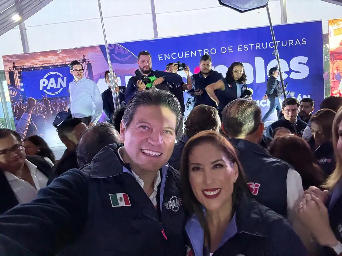 Personas en evento político con logotipo de PAN y fondo con cartel de encuentro de estructuras.
