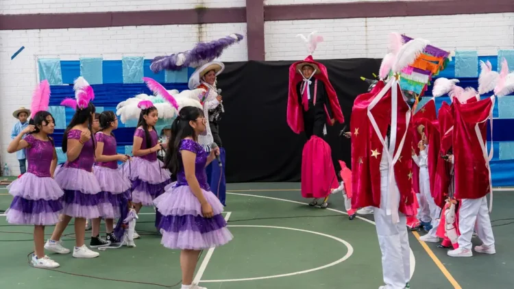 Niñas y niños en presentación teatral con disfraces coloridos en un gimnasio de Tlaxcala.