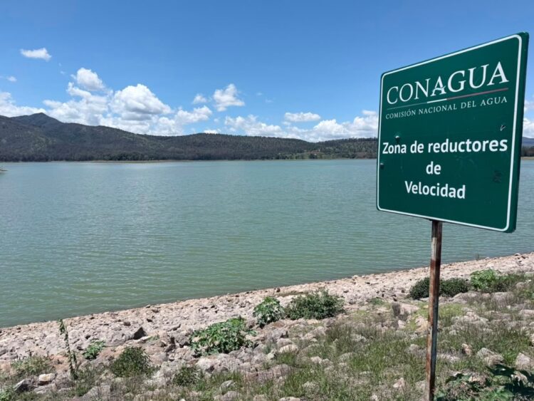Cartel de Conagua indicando zona de reductores de velocidad junto a un lago y montañas.