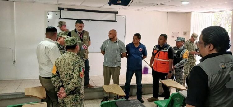 Varias personas, incluyendo militares y personal de protección civil, están reunidas en un aula escolar.