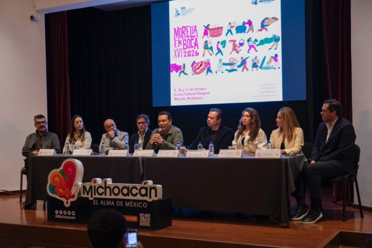 Un grupo de nueve personas está sentado en una mesa en un escenario durante una conferencia, con un cartel de “Morelia en Boca 2026” proyectado detrás.