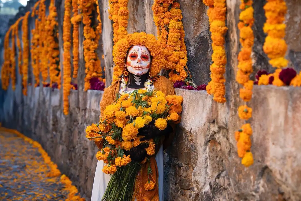 Muñeca con maquillaje de calavera y flores de cempasúchil en celebración de Día de Muertos en Michoacán.