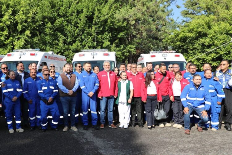 Grupo de paramédicos y personal de emergencias frente a ambulancias en un área verde.