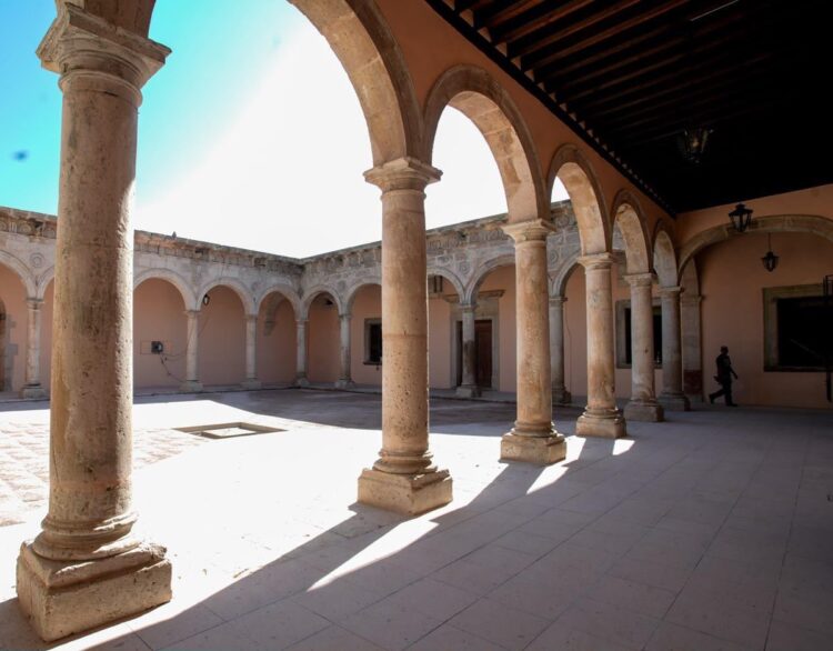 Patio colonial con arcos de piedra y columnas en Michoacán, iluminación natural y fondo de cielo azul.