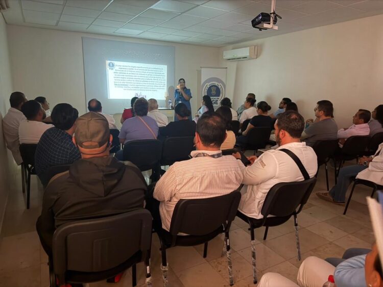 Funcionarios públicos en capacitación sobre seguridad en una sala de reuniones con proyector y pantalla.