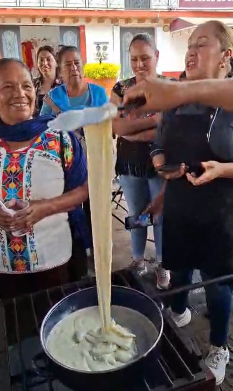 Varias personas observan mientras alguien estira queso derretido desde una olla en un entorno al aire libre.