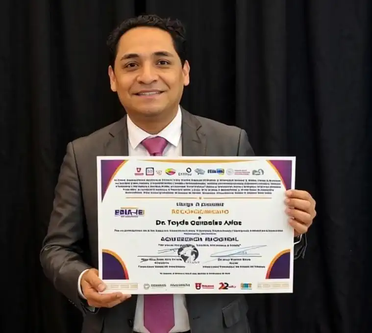 Hombre con traje sostiene certificado en un escenario con fondo negro.