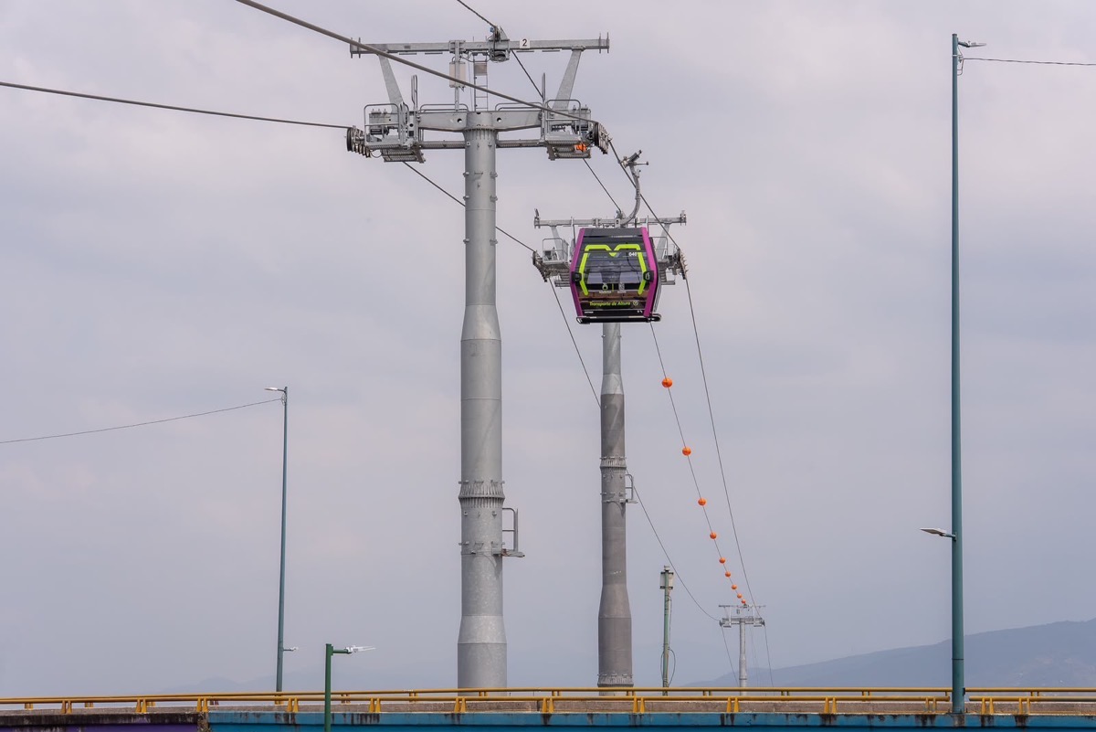 Teleférico en construcción en Michoacán, con cabina suspendida y cables en un día nublado.