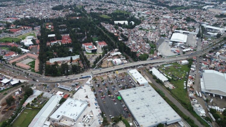 Vista aérea de una ciudad con edificios, calles, estacionamientos y áreas residenciales rodeadas de vegetación.