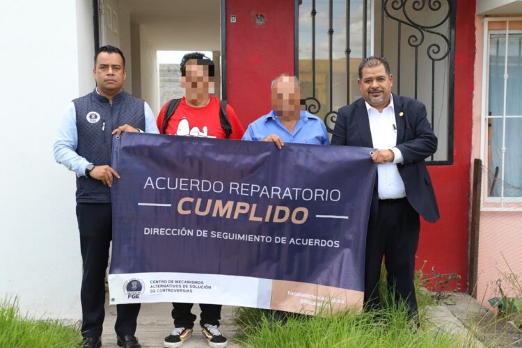 Cuatro hombres posan frente a una casa sosteniendo una pancarta que dice “Acuerdo reparatorio cumplido”.