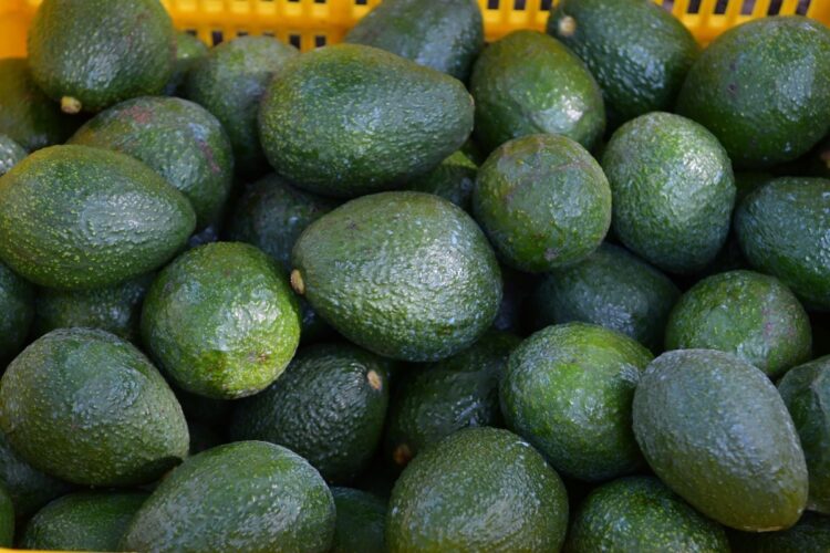 Un montón de aguacates verdes apilados en una canasta amarilla.