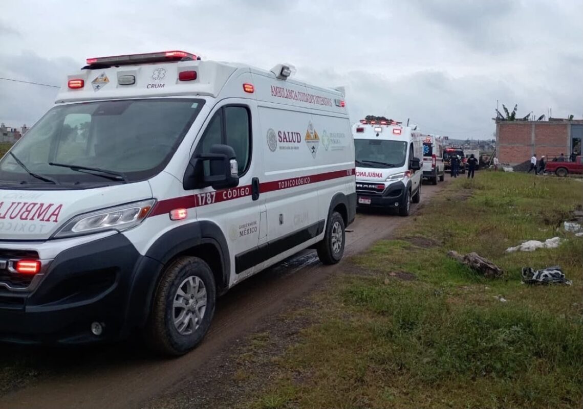 Varias ambulancias están estacionadas en un camino de tierra cerca de un edificio y un grupo de personas.