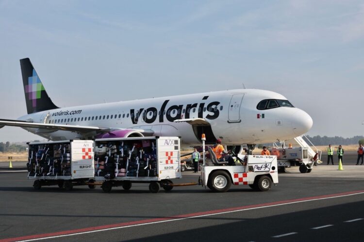 Un avión de Volaris está en la pista mientras personal carga el equipaje en carritos.