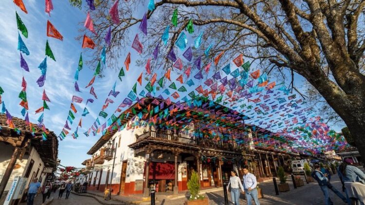 Calle adoquinada con casas coloniales decorada con banderines de colores colgantes y personas caminando.