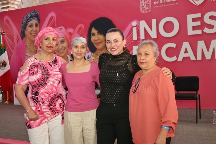 Cuatro mujeres posan sonrientes frente a un fondo rosa en un evento, con dos de ellas usando pañuelos en la cabeza.