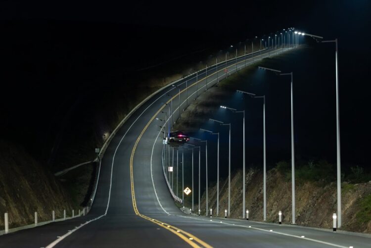 Una carretera iluminada por farolas se curva y sube por una colina durante la noche.